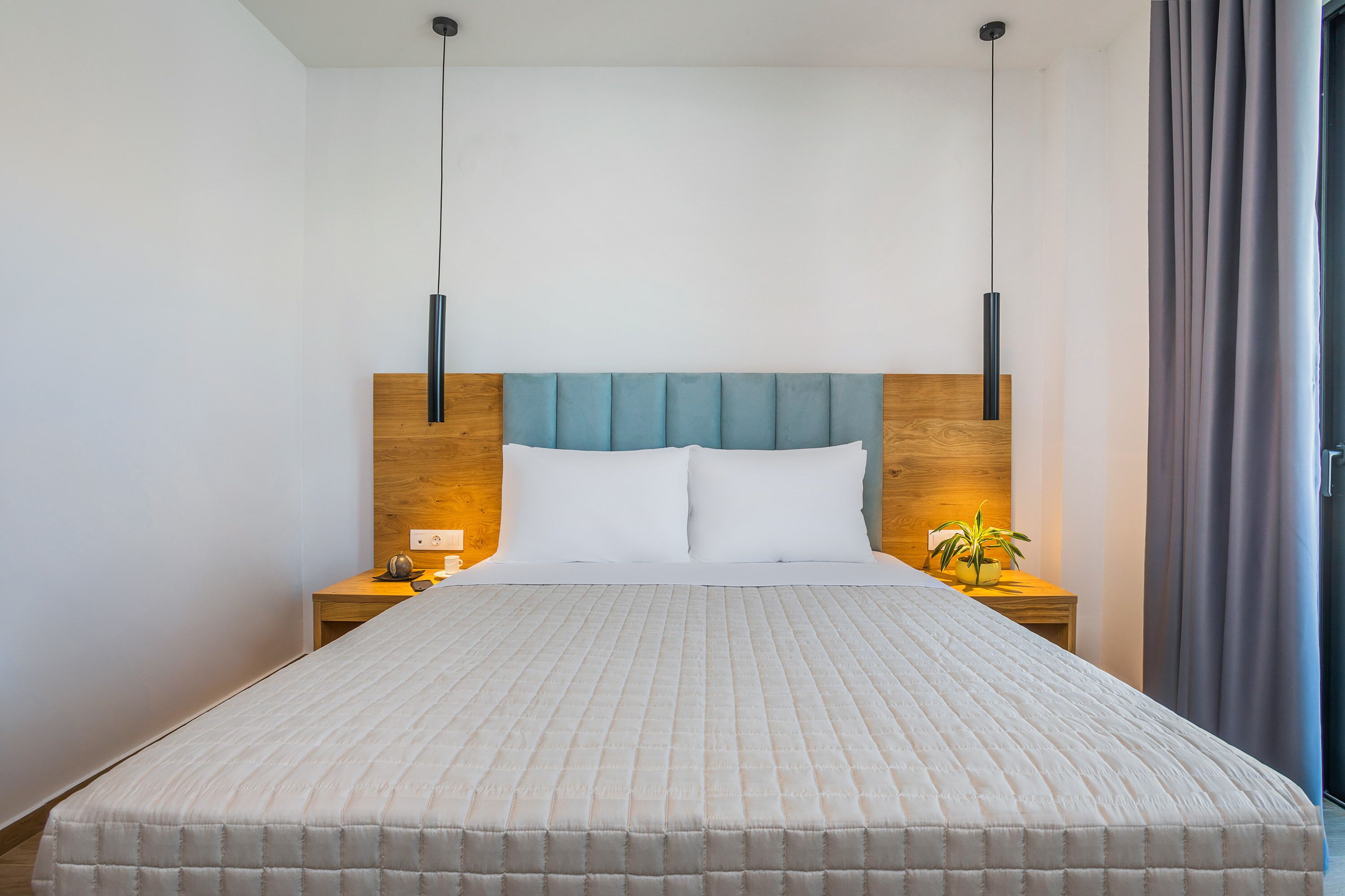 A neatly made bed with a wooden headboard and two bedside tables, each with a lamp and a small plant.