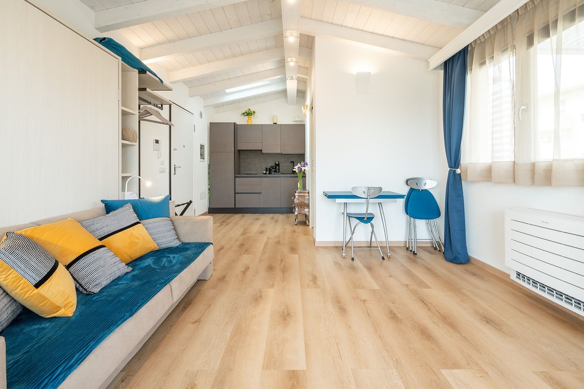 Una sala de estar moderna con un sofá, un comedor con sillas y una cocina al fondo.