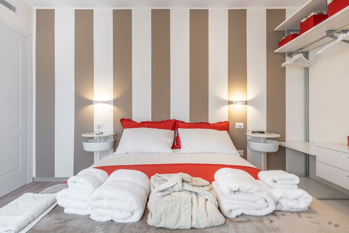 Una habitación de hotel con una cama, dos mesitas de noche, un espejo y una pared a rayas rojas y blancas.