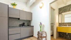 A modern kitchen with grey cabinets, a coffee machine, and a vase with flowers on a small table. - Le Residenze di Carlà (Cagliari)