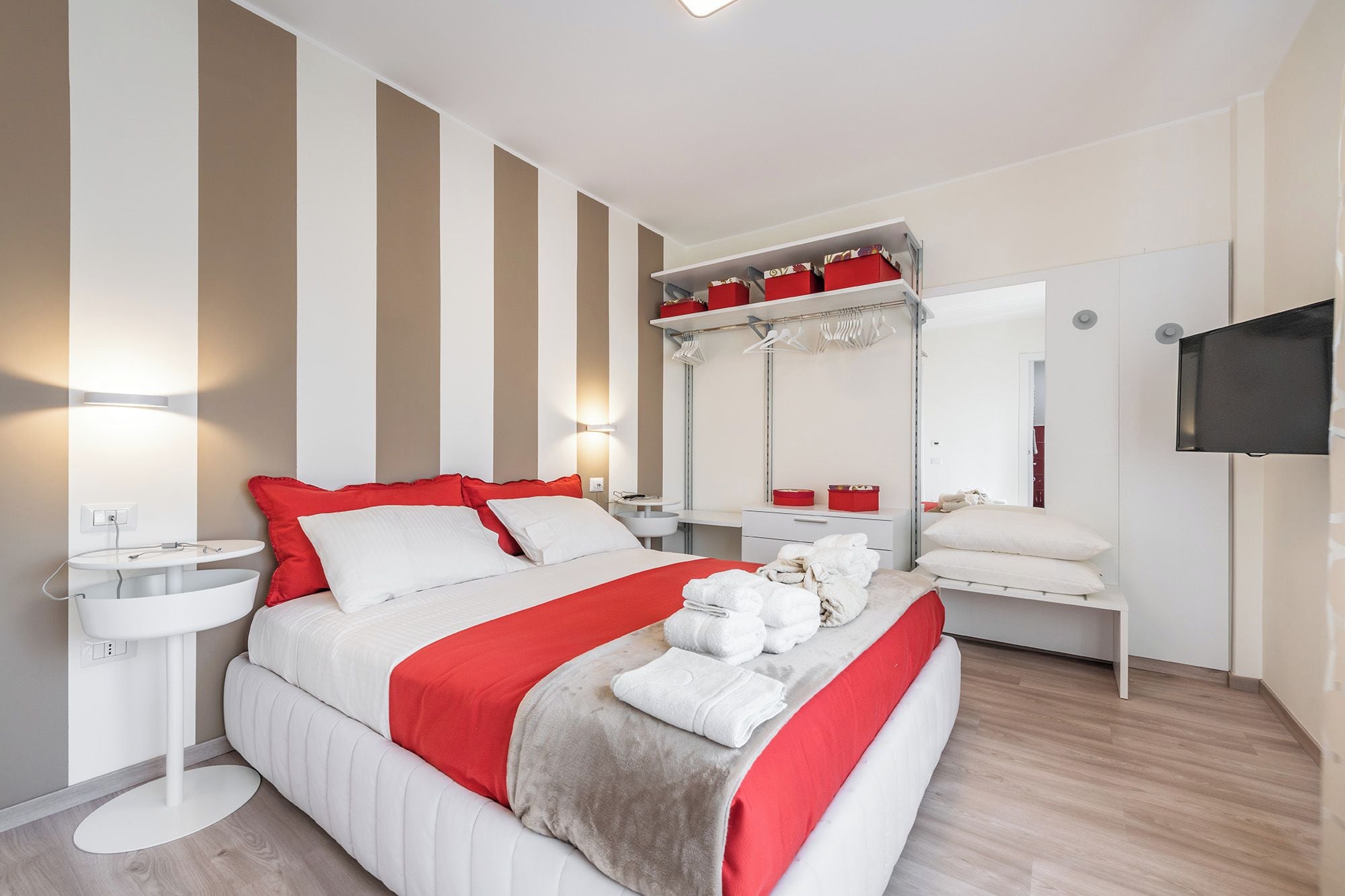 A hotel room with a bed, bedside tables, a mirror, a TV, and a wardrobe.