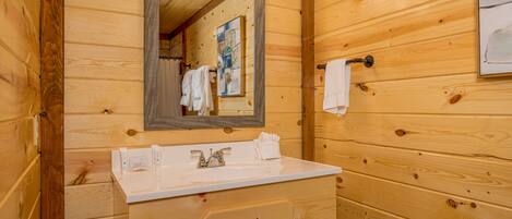A wooden cabin-style bathroom with a white sink, a mirror, and a towel rack.
