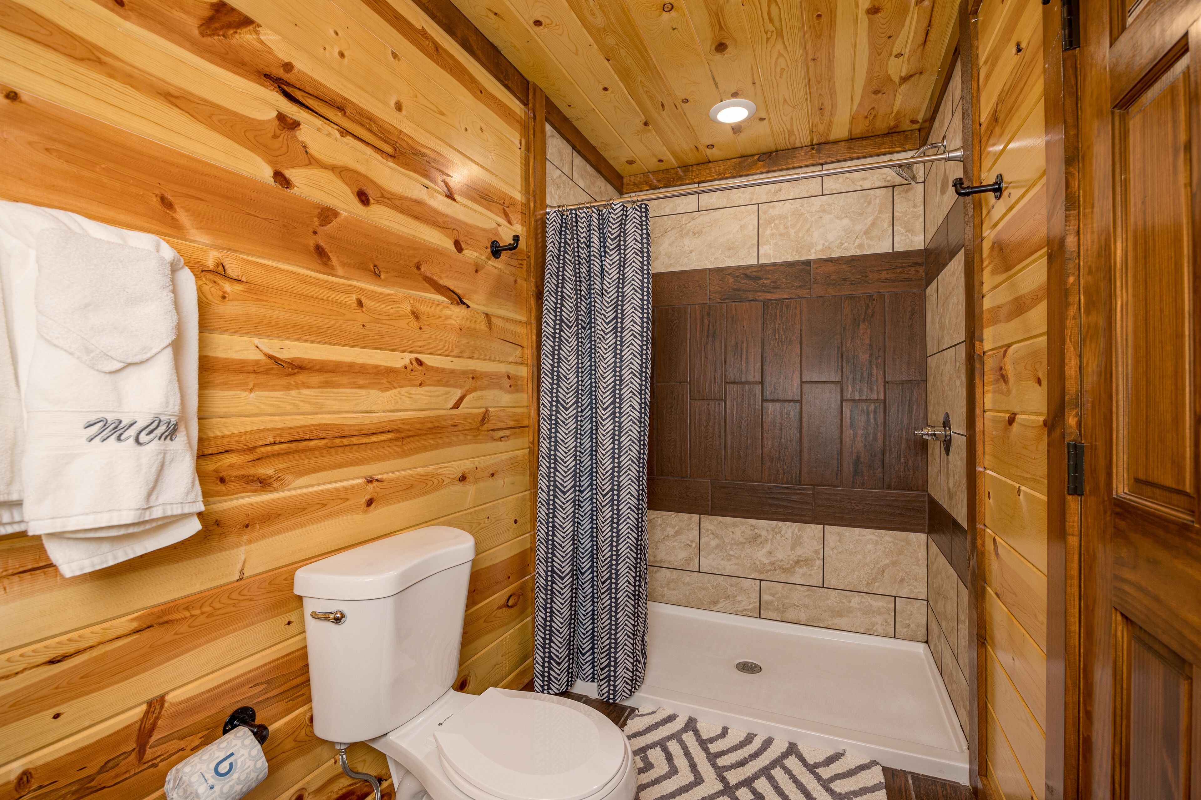 Un interior de madera con un inodoro, una ducha con cortina estampada y un perchero para toallas.