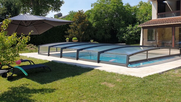 A swimming pool with a glass enclosure, surrounded by a grassy lawn and a patio area. - South-facing detached house with private pool (Puy-l'Évêque)