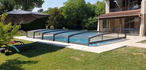 A swimming pool with a glass enclosure, surrounded by a grassy lawn and a patio area.