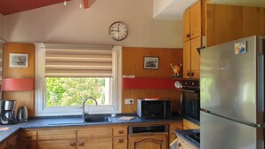 A kitchen with wooden cabinets, a stainless steel refrigerator, a microwave, and a sink with a window above it. - South-facing detached house with private pool (Puy-l'Évêque)