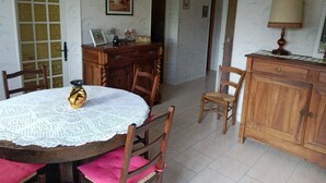 A dining area with a round table, chairs, a wooden cabinet, and a door leading to another room. - Les Cigales II (Lamothe-Fénelon)