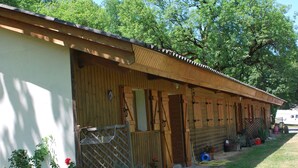 A row of wooden cabins with a covered entrance, a fenced area with potted plants, and a grassy lawn. - Les Cigales II (Lamothe-Fénelon)