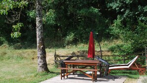 A wooden deck with a table and chairs, surrounded by trees. - Les Cigales II (Lamothe-Fénelon)