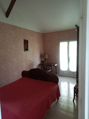A bedroom with a bed, a chair, a table, and a door leading to a balcony.