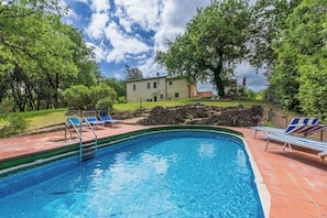 A swimming pool with blue lounge chairs, a stone wall, and a building in the background.