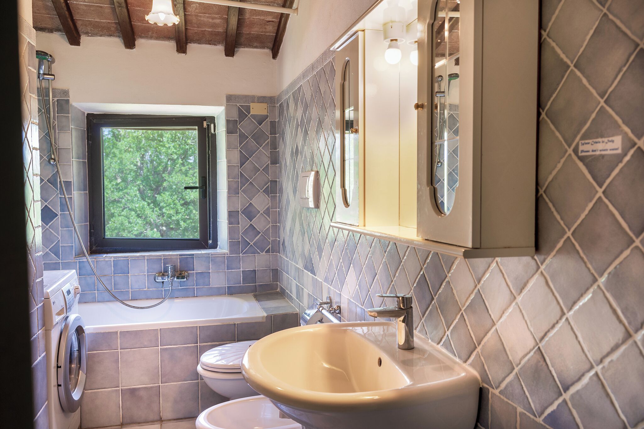 A bathroom with a window, a bathtub, a sink, and a washing machine.