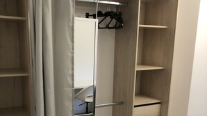 Een inloopkast met open planken, een spiegel en een kapstok.