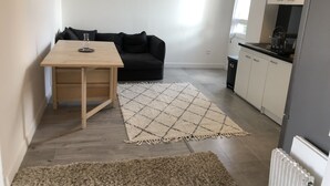 Een compacte leefruimte met een kitchenette, een eettafel, een bank en een groot vloerkleed.