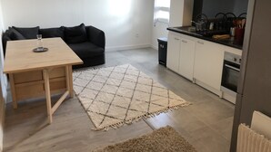 Een moderne keuken met witte kasten, een zwart aanrecht en een ingebouwde oven. Er staat een zwarte bank en een houten tafel met een glazen vaas.