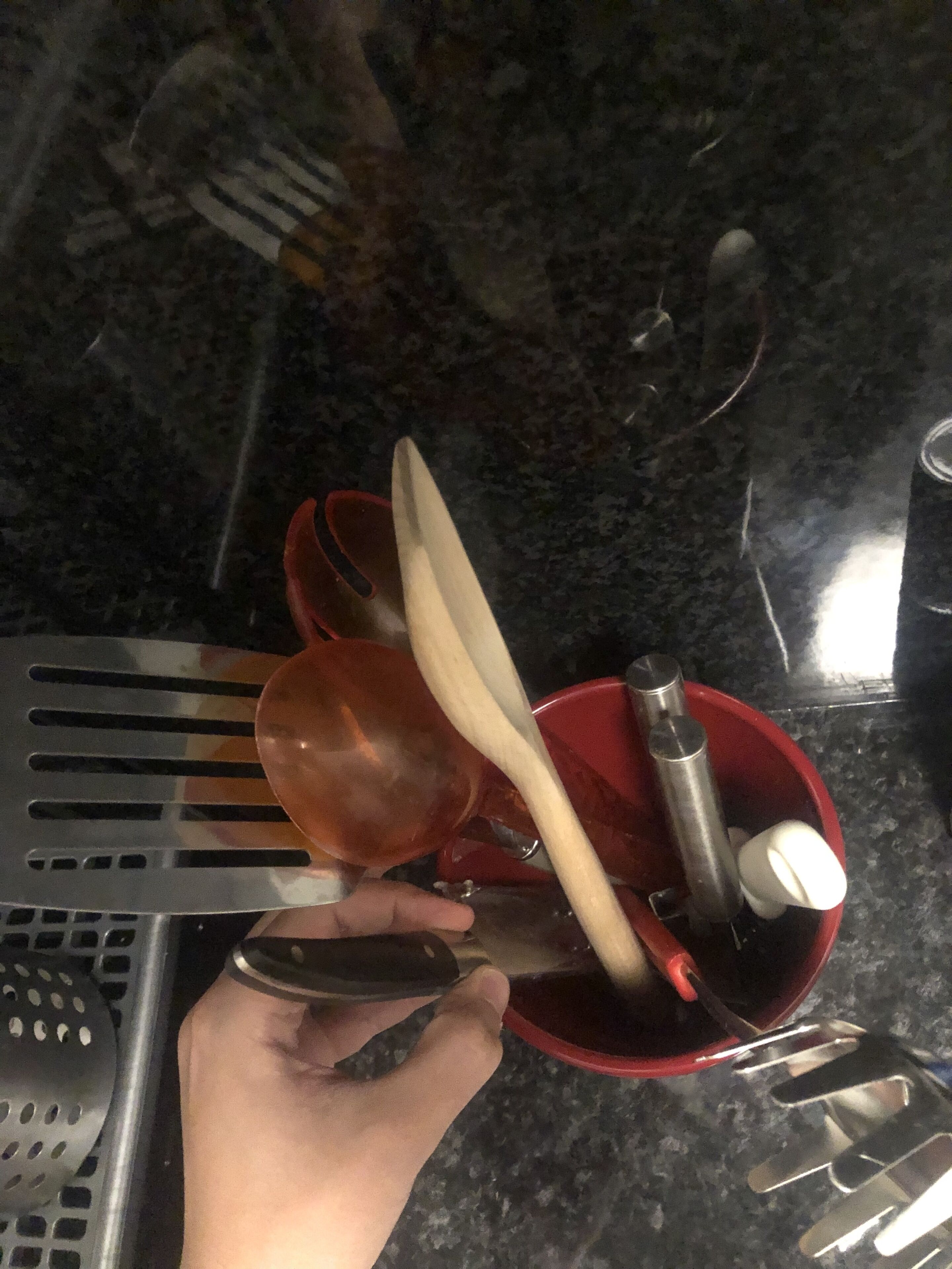 Une main tenant un bol rouge avec une cuillère et une spatule.