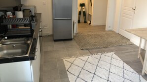 Een keuken met een koelkast van roestvrij staal, een spoelbak en een magnetron. Er ligt een vloerkleed op de vloer en een deur die naar een andere kamer leidt.