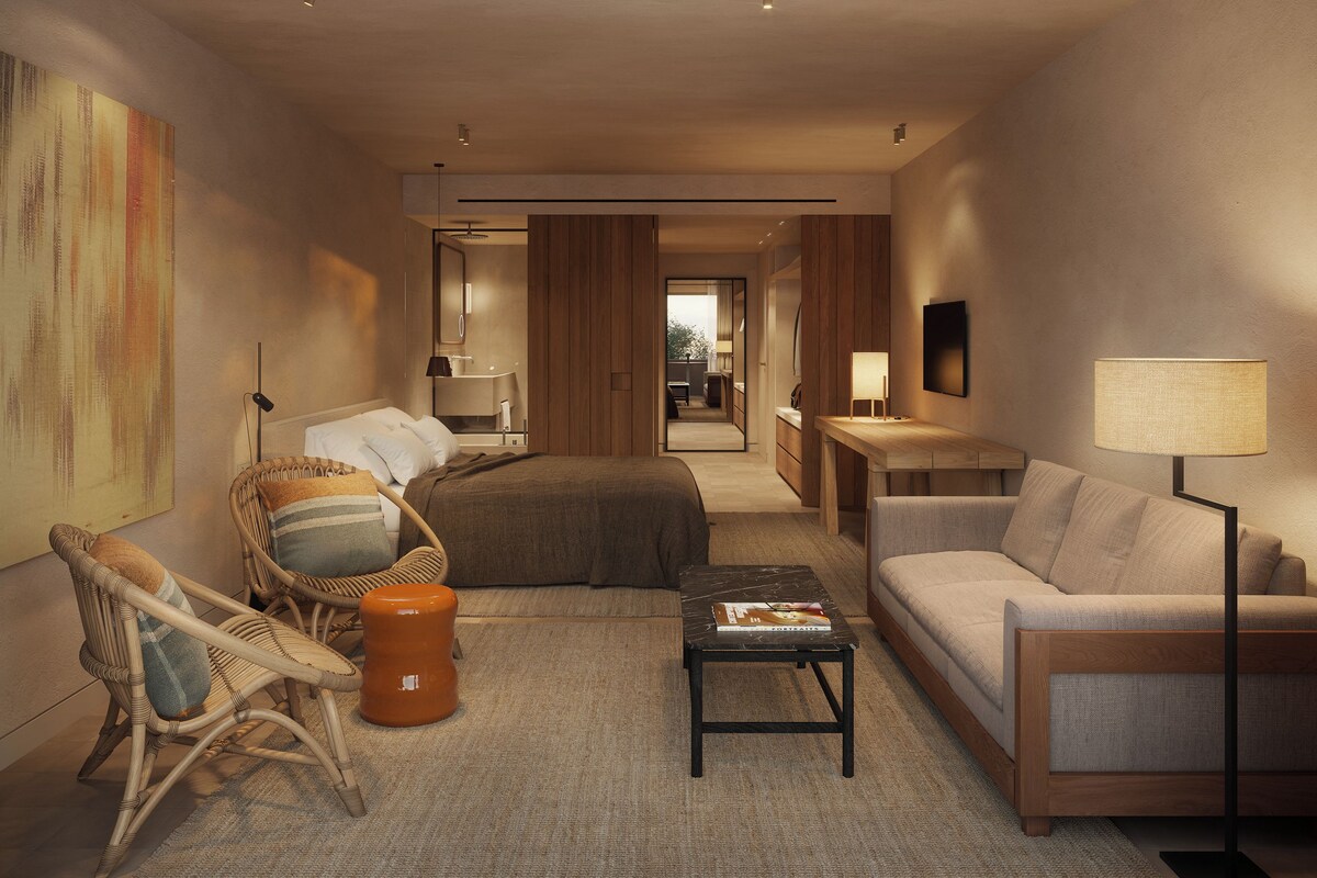 A modern hotel room with a bed, seating area, and a view into the bathroom.