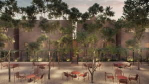 Un espacio al aire libre con mesas y sillas, rodeado de árboles y un edificio al fondo.