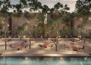 Un espacio al aire libre con mesas y sillas, rodeado de árboles y un edificio al fondo.