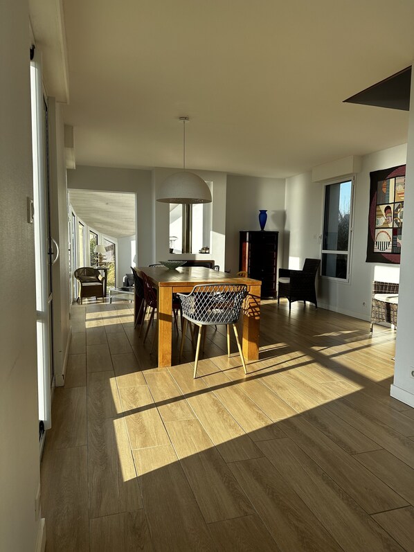 Un vaste espace de vie comprenant une table à manger en bois, un luminaire suspendu moderne et une vue sur l’extérieur.
