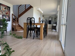 Un espace repas avec une table et des chaises en bois, un escalier et une cuisine en arrière-plan.