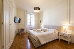 Hotellihuone, jossa on sänky, yöpöydät, televisio, tuoli ja ikkuna.