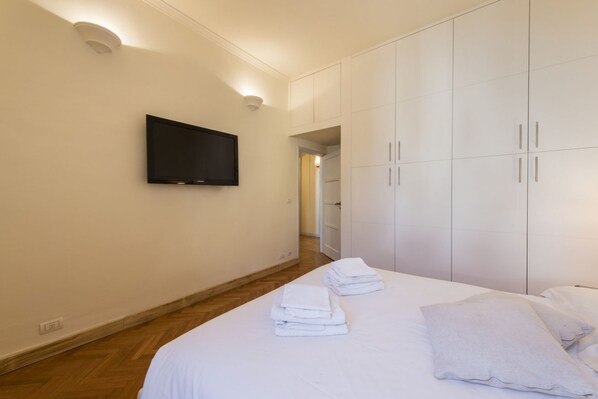 A hotel room with a bed, a TV mounted on the wall, and a wardrobe.