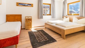 Habitación de hotel con dos camas, cabecera de madera, cesta de mimbre, vista a las montañas a través de la ventana y un cuadro en la pared.
