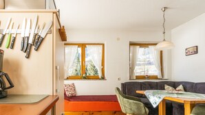 Un salón acogedor con suelo de madera, un sofá, una mesa de comedor y una zona de cocina con cuchillos colgados en la pared.