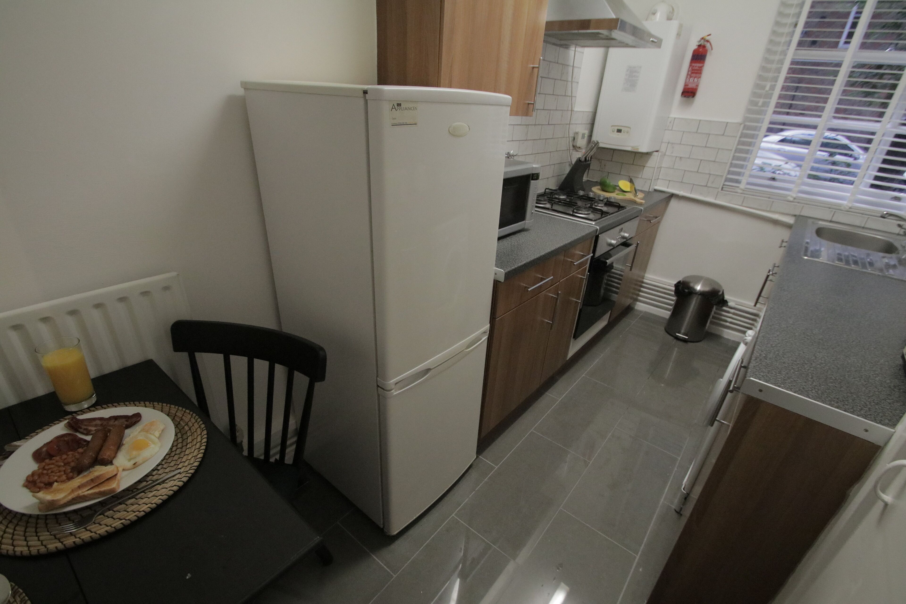 Eine kleine Küche mit Kühlschrank, Herd und Spüle. Ein Esstisch mit einem Teller Essen und einem Stuhl sind ebenfalls vorhanden.
