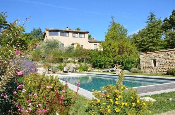 A pool area with a stone wall, surrounded by lush greenery and flowering plants.