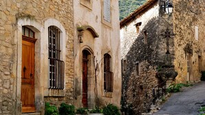 A narrow street with stone buildings, wooden doors, and a cobblestone path. - In the heart of the Grand Luberon, a SWIMMING POOL, a QUIET, comfortable home. (Castellet-en-Luberon)