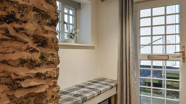 A room with a stone wall, a bench with a checkered cushion, a window with a view, and a door with a metal handle. - 1 bedroom accommodation in Cemaes Bay (Cemaes Bay)