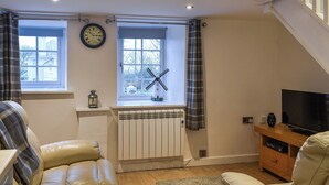 A cozy living room with a sofa, a television, a radiator, and a window with curtains. - 1 bedroom accommodation in Cemaes Bay (Cemaes Bay)