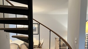 En trappa med ett träräcke och steg klädda med matta, som leder upp till en matplats med flätade stolar och ett bord.