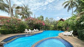 Una piscina con dos zonas diferenciadas, rodeada de palmeras y abundante vegetación.