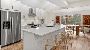Een moderne keuken met witte kasten, roestvrijstalen apparatuur en een groot kookeiland met barstoelen.