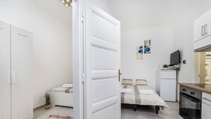 A compact room with a bed, a small kitchenette, and a door leading to another room. - Real Apartments Kertész II. (Budapest)