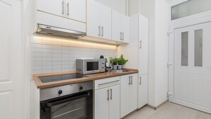 A modern kitchen with white cabinetry, a built-in oven, a microwave, and a stainless steel range hood. - Real Apartments Kertész II. (Budapest)