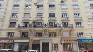 A multi-story building with a central entrance, balconies with plants, and storefronts including a restaurant and a cultural bar. - Real Apartments Kertész II. (Budapest)
