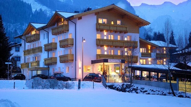 A multi-story hotel with balconies, a covered parking area, and a view of snow-covered mountains. - Apartment in Neustift Near Ski Lift (Neustift Im Stubaital)