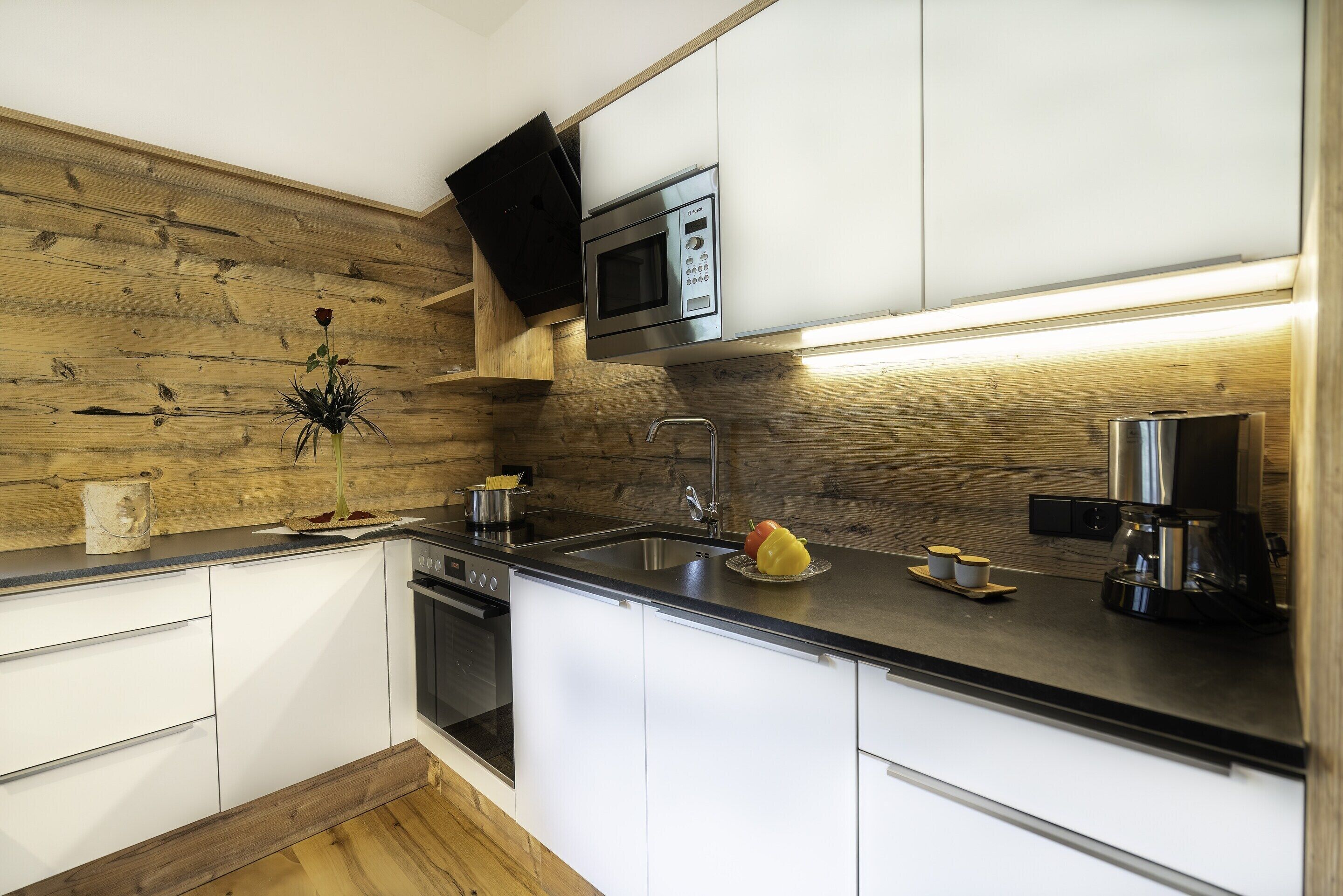 A modern kitchen with white cabinets, a stainless steel microwave, and a wooden backsplash.