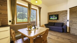 A dining area with a wooden table and chairs, a wooden floor, a sofa, and a TV mounted on a wooden wall. - Apartment in Neustift Near Ski Lift (Neustift Im Stubaital)