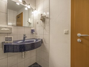 Un baño con lavamanos de granito, un espejo, un secador de pelo y dispensador de toallas.