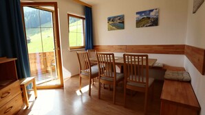 A dining area with wooden furniture, a large window with a view of a green landscape, and two paintings on the wall. - Holiday Apartment in Stubai With Balcony (Neustift Im Stubaital)