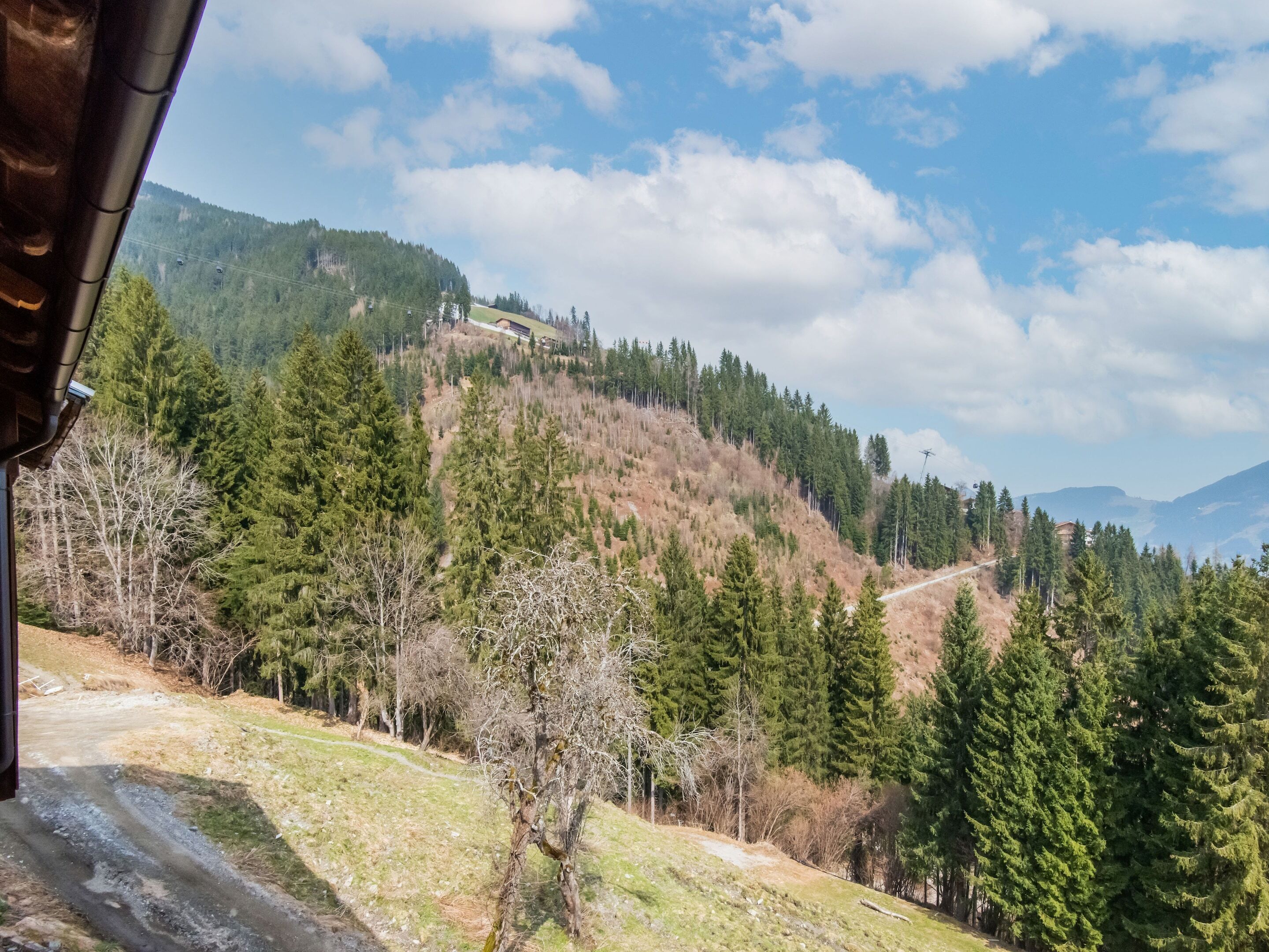 Un paysage de montagne avec un chalet perché sur une colline, entouré de forêts denses et sous un ciel dégagé.