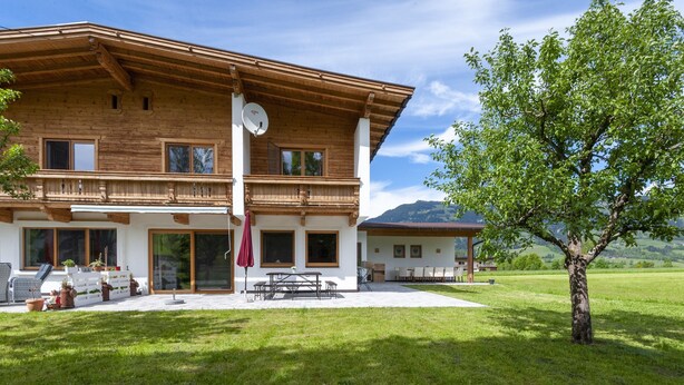 A two-story wooden house with a patio, outdoor seating, and a view of the surrounding landscape.