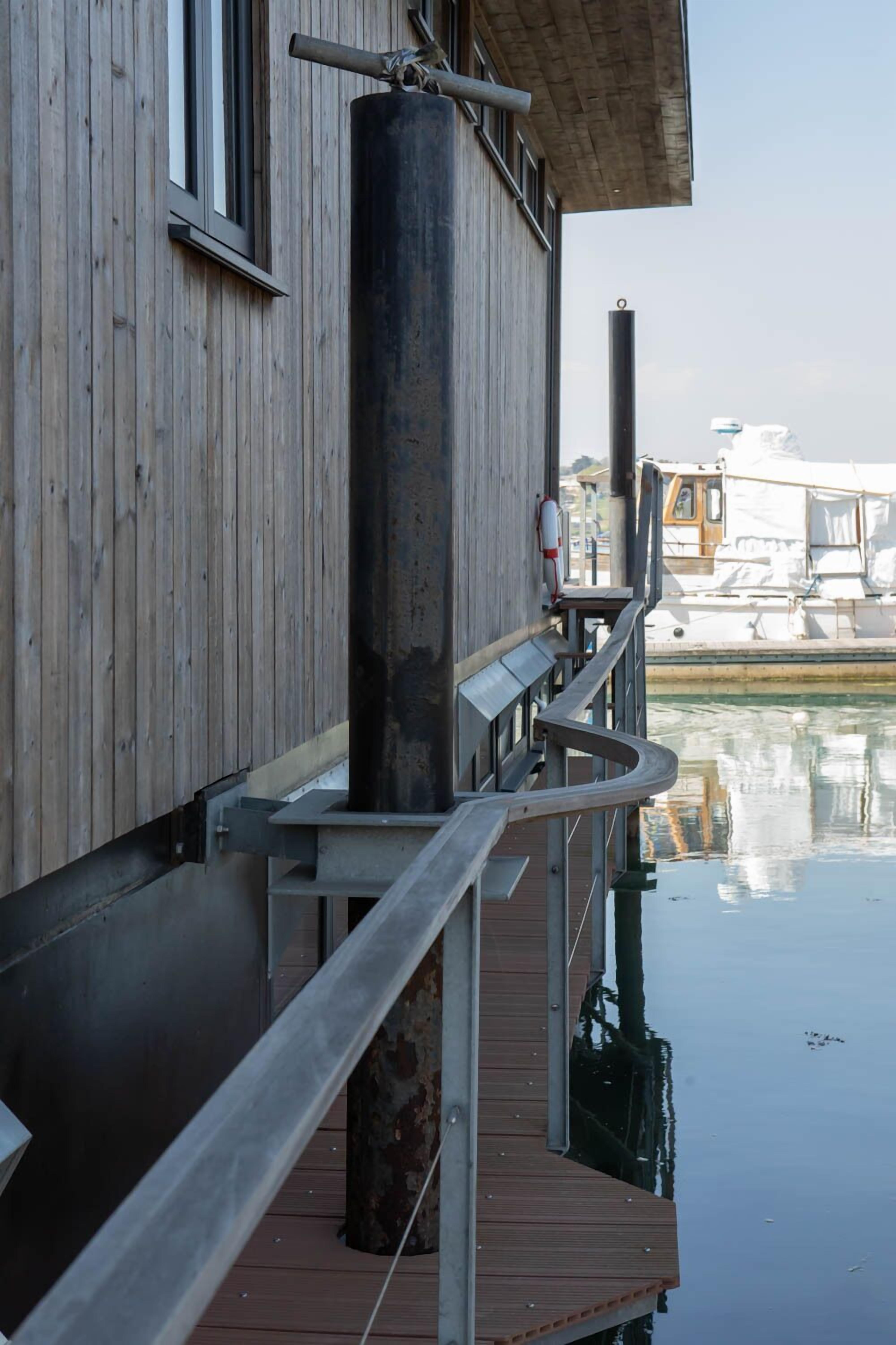 A wooden dock extending into a calm body of water, with a metal railing and a cylindrical structure nearby.