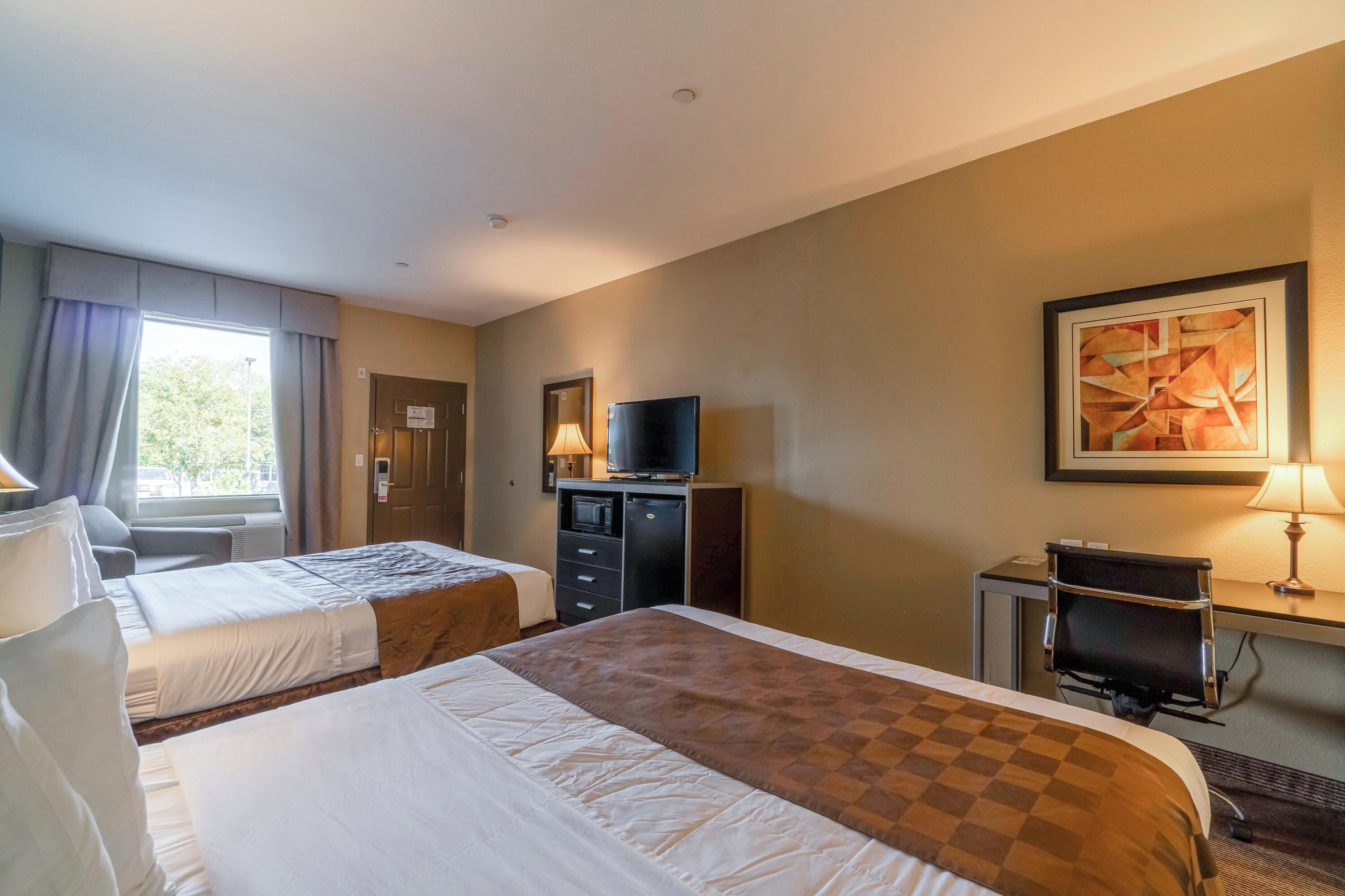 Quarto de hotel com duas camas, uma escrivaninha, uma televisão e um quadro na parede.